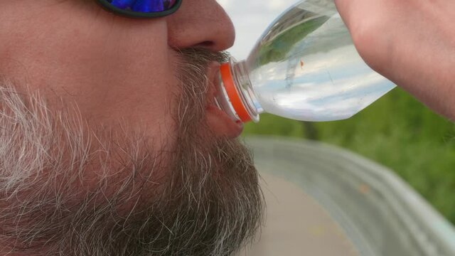 Clos eup of man's face in suglasses who drinks water from plastic bottle. Bicycle rider is thursty.