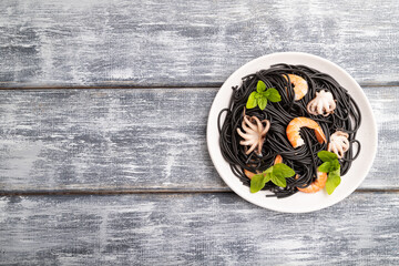 Black cuttlefish ink pasta with shrimps or prawns and small octopuses on gray wooden background. Top view, copy space.