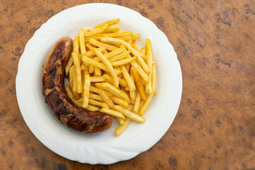 Grilled sausage, German Bratwurst, and french fries on a plate in a fast food restaurant, tasty but unhealthy eating with trans fat and saturated fatty acids, copy space, high angle view from above