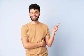 Young Moroccan man isolated on blue background happy and pointing up