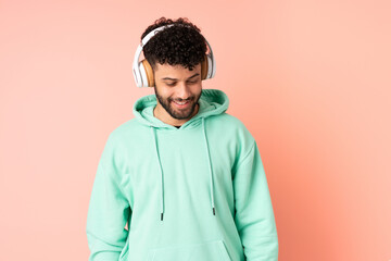 Young Moroccan man isolated on pink background listening music