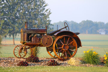 a rusty vintage farm tractor on display in a rural farm with bright flowers early morning