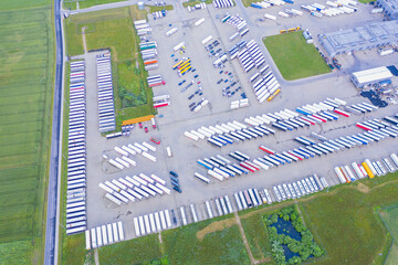 Lots of freight trailers. Cars are in several rows. Truck parking. Aerial view vertically down.