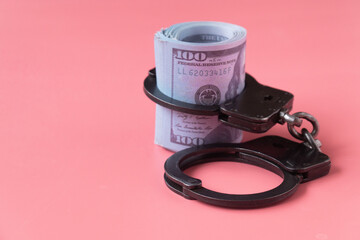 twisted wad of dollars buttoned with handcuffs on a pink background