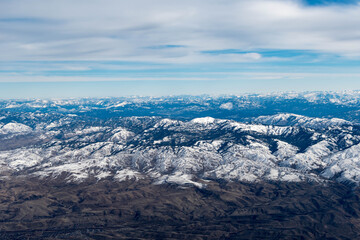 Obraz premium Aerial View of Idaho mountains from the sky while inside an airplane. View of brown mountains and trees covered with snow