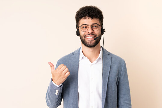 Telemarketer Moroccan man working with a headset isolated on beige background pointing to the side to present a product