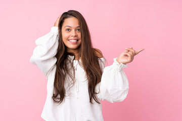 Young Brazilian girl over isolated pink background surprised and pointing finger to the side