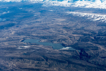 Aerial View of Idaho mountains and lake lowell from the sky while inside an airplane. View of brown mountains and trees covered with snow