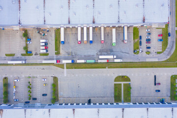 Aerial view of goods warehouse. Logistics center in industrial city zone from above. Aerial view of trucks loading at logistic center. View from drone.