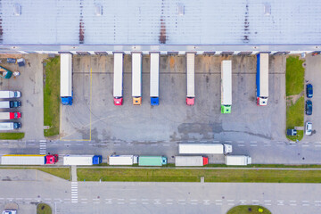 Aerial view of goods warehouse. Logistics center in industrial city zone from above. Aerial view of trucks loading at logistic center. View from drone.