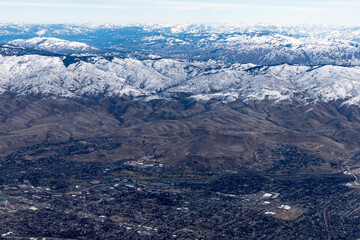 Aerial View of Idaho mountains from the sky while inside an airplane. View of brown mountains and trees covered with snow