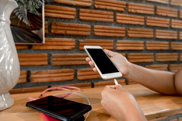 The hand of a young woman holding a smartphone and a modern spare battery charger Place the lap to charge the smartphone with a spare battery charger and play on a chair in the room