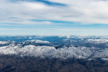 Aerial View of Idaho mountains from the sky while inside an airplane. View of brown mountains and trees covered with snow