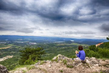 Naklejka premium Eine junge Frau isst brot auf dem gipfel unter dicken wolken im blauen pullover