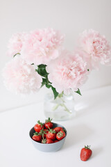 Obraz na płótnie Canvas Pink peonies in a vase and strawberries on the table. Beautiful fresh cut bouquet. Home house interior. Summer day. Copy space