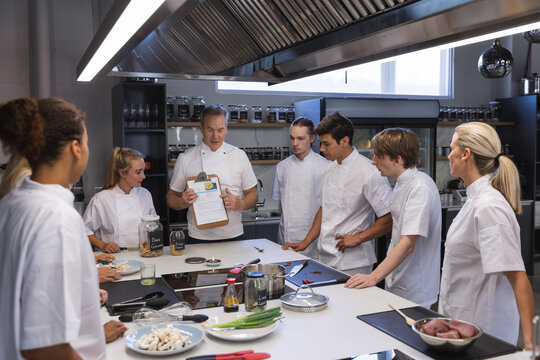 Senior male chef showing paper to all other chefs at restaurant kitchen