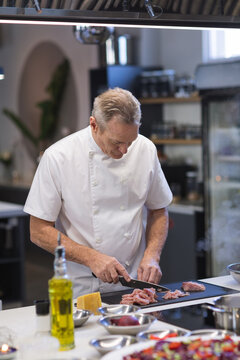 Senior male chef cutting meat at restaurant kitchen