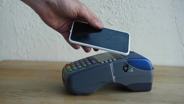 cropped view of man applying smartphone to payment terminal and pushing buttons