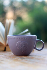 Purple cup of tea or coffee and open book in a garden. Selective focus.