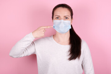 Portrait of a brunette girl in a medical mask, pointing with finger on face.