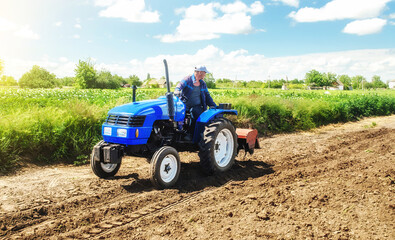 Fototapeta premium A farmer rides across the field on a tractor with a milling machine. Loosening surface, cultivating land for planting. Farming and agriculture. Work on the farm. Ground preparation for crop planting.