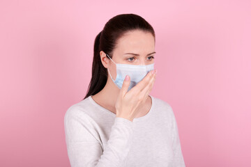 Portrait of a brunette girl in a medical mask coughs. Isolated on pink background.