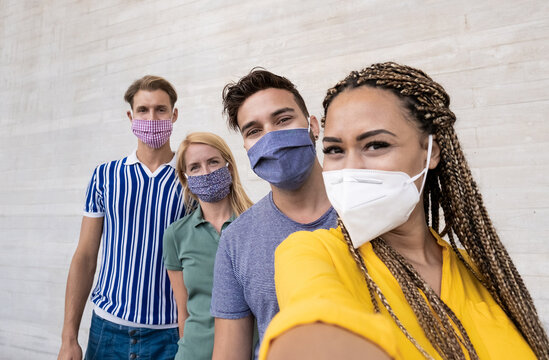 Happy multiracial friends taking a selfie and wearing protective face masks - Concept of health care and the new normality - Focus on the men on the right