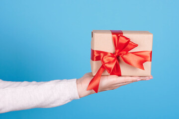 Present box with red ribbon in hand on blue background.