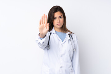 Teenager girl over isolated white background wearing a doctor gown and making stop sign