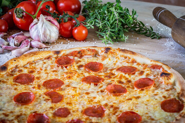 Pepperoni pizza and cooking ingredients: tomatoes, basil, garlic on wood table background