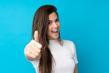 Fototapeta premium Teenager girl over isolated blue background with thumbs up because something good has happened