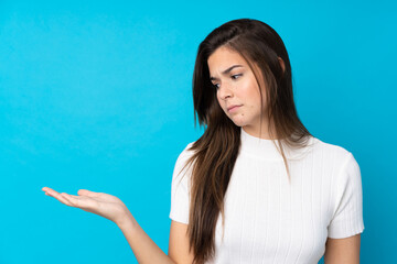 Fototapeta na wymiar Teenager girl over isolated blue background holding copyspace with doubts