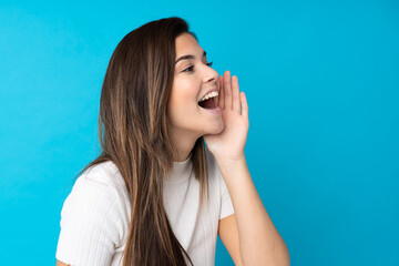 Fototapeta premium Teenager girl over isolated blue background shouting with mouth wide open to the lateral
