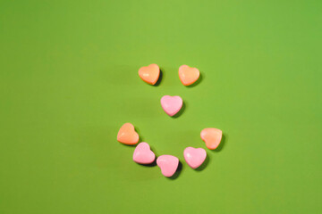  smiling face made of colored sweets in the shape of hearts green background         