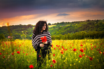 Young woman in a field of red poppies at sunset