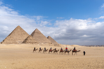 Giza, Cairo, Egypt - 02 08 2020: Camel ride across a desert at the great pyramids of Giza. Clear sky and cool weather.