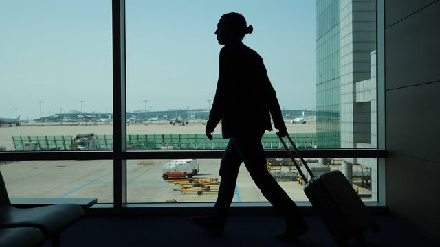 Man walk with trolley case at lounge, silhouetted slow motion shot against window. Boarding begin and gate open, passenger come to airliner. Modern international airport terminal