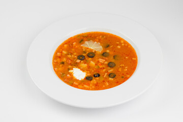 Solyanka. Solyanka in a white plate. Solyanka with sauce and lemon.