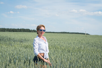 Naklejka na ściany i meble stylish woman in a white shirt and jeans shorts walks on a wheat field