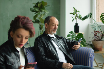 Family portrait of adult daughter and senior father in loft room with houseplants. Man and girl are...