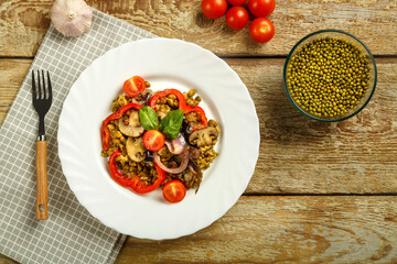 On a wooden table is a white dish of boiled mung bean with mushrooms and vegetables on a napkin and a fork next to the ingredients.