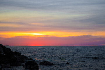 Fototapeta na wymiar colorful yellow pink sunset on rocky beach with cloudy sky