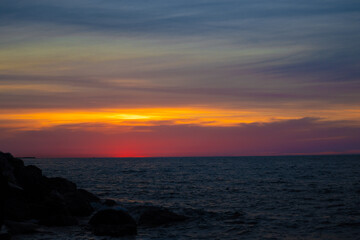 colorful yellow pink sunset on rocky beach with cloudy sky