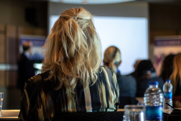 Blonde female person attended to a meeting, people are listening the presentation