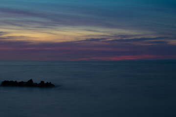 colorful purple pink sunset on rocky beach with cloudy sky