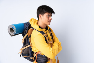 Young mountaineer man with a big backpack over isolated blue background laughing