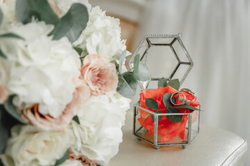 Wedding bouquet and rings on a red flower in a glass box.