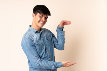 Handsome man over isolated beige background holding copyspace to insert an ad