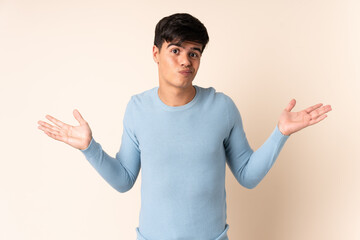 Handsome man over isolated beige background having doubts while raising hands