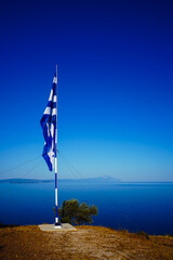 Greek flag standing on a hill against the background of the Mediterranean Sea and Mount Athos.